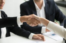 two people shaking hands in front of a laptop
